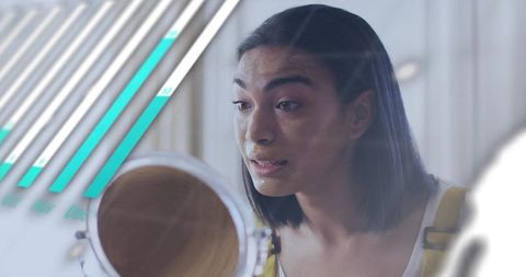 Young woman examining skin in vanity mirror, applying skincare with soft teal light overlay
