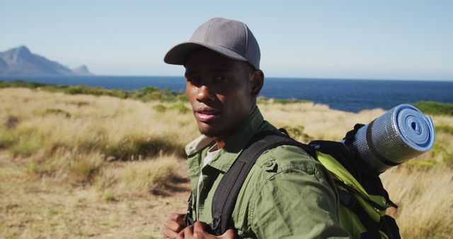 Young man hiking near the ocean with backpack, enjoying nature. Ideal for outdoor adventure activities, travel blogs, camping gear advertisements, and lifestyle promotions.