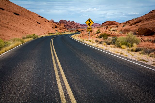 Desert road winding through red rock formations, ideal for travel blogs, tourism ads, and road trip articles. Suitable for illustrating adventure, exploring remote locations, and scenic drives across vast open landscapes.