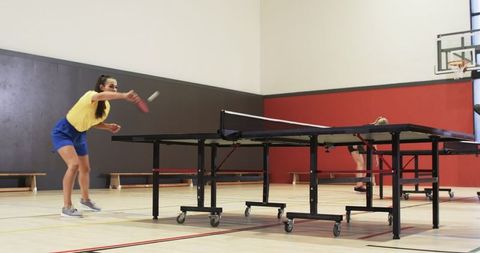 Two Women Energetically Playing Table Tennis in Gymnasium