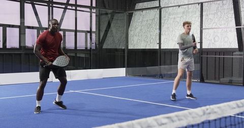 Diverse sportsmen on indoor padel court preparing to play