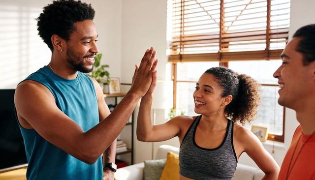 Sunlit home workout friends high-fiving after exercise session in living room celebrating