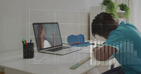 Student studying at home desk using laptop tutor while writing homework in neat workspace