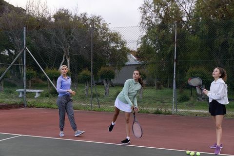 Women practicing tennis together on outdoor court during overcast day