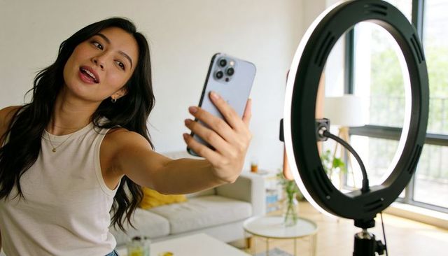 Asian woman vlogging with smartphone and ring light in modern living room for creators