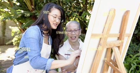 Senior and young woman painting together in garden during outdoor art lesson and mentoring