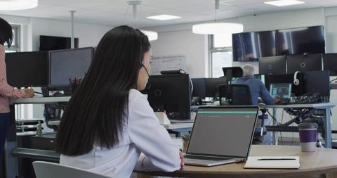 Headset-wearing professional typing on laptop in open-plan office coworking workspace