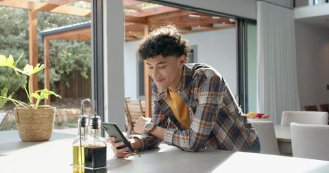 Young Man Using Smartphone in Modern Kitchen with Sunlight