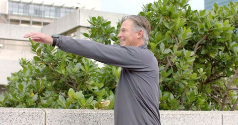 Mature man stretching arms on urban terrace with smartwatch