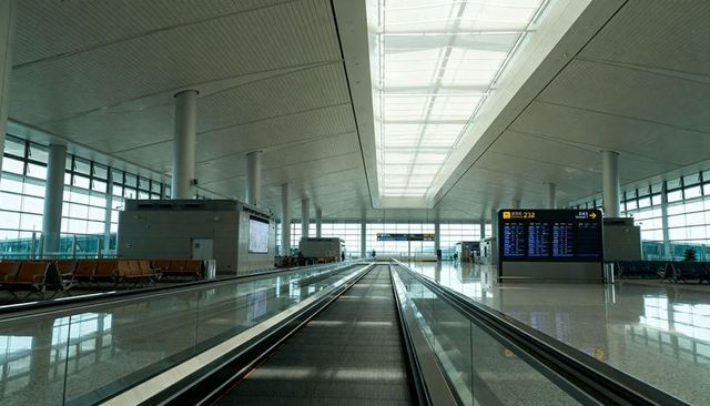 Leading moving walkway in modern airport concourse with skylight, departure display and seating