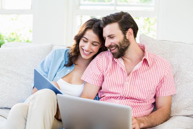 Happy couple sitting on sofa using digital tablet and laptop in living room