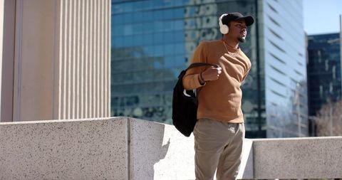African American commuter standing on urban terrace wearing headphones and backpack