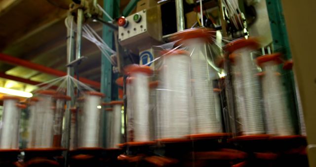 Close-up of spinning machinery in textile factory focusing on yarn spools during manufacturing process. Ideal for illustrating concepts related to industrial automation, textile production, and the mechanics of manufacturing facilities.