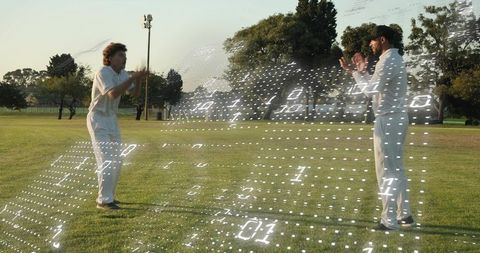 Cricket teammates clapping on grassy field with holographic digital grid overlay at sunset