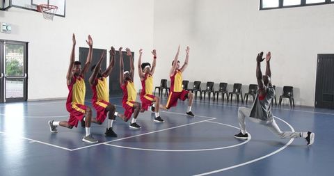 Basketball Team Practicing Lunges with Coach on Indoor Court