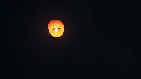 Orange Paper Lantern Floating and Rotating Over Night Sky with Warm Internal Flame