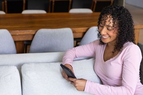 Relaxed Young Woman Joyfully Browsing Phone in Cozy Living Room