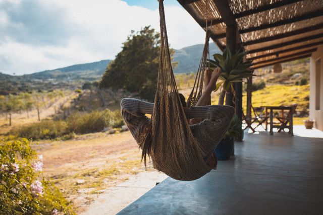 Caucasian woman relaxing while lying in a hammock on porch of wooden house near the mountains. adventure, lifestyle and travel concept