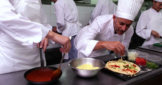 Professional chefs are preparing pizza in a bustling restaurant kitchen. The image showcases them working together, assembling ingredients with precision. This is ideal for articles, advertisements, or content related to culinary arts, restaurant management, teamwork, and professional cooking techniques.