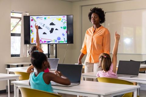 Black Teacher Leading Tech-Enabled Elementary Classroom With Laptops and Interactive Screen