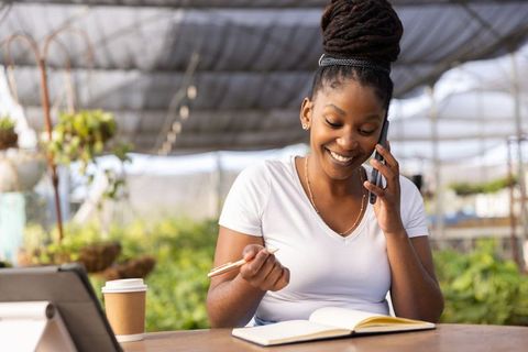 African american woman managing plant nursery, taking notes and talking on phone