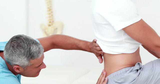 A middle-aged Caucasian male chiropractor is examining the lower back of a patient, with copy space. Chiropractic care is often sought for back pain relief and spinal adjustments.