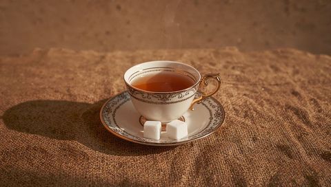 Vintage gold-rimmed porcelain teacup with amber tea and sugar cubes on burlap tabletop
