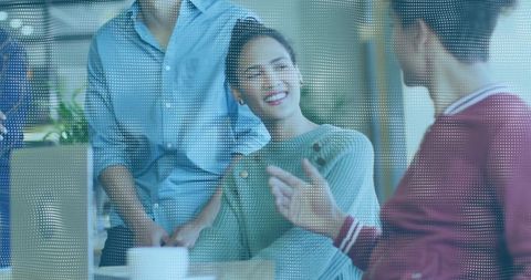 Smiling woman engaging in informal coworking discussion through dotted glass partition