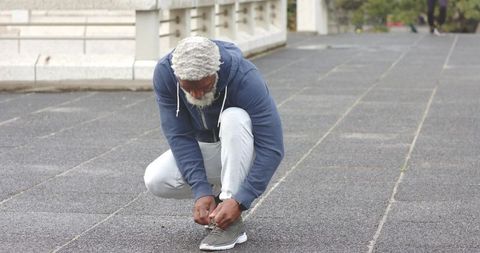 Senior african american man tying sneakers on urban walkway during morning exercise