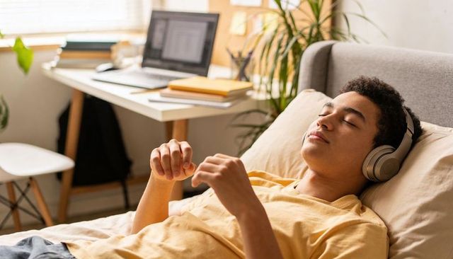 Young man relaxing on bed listening with headphones in sunlit minimalist bedroom