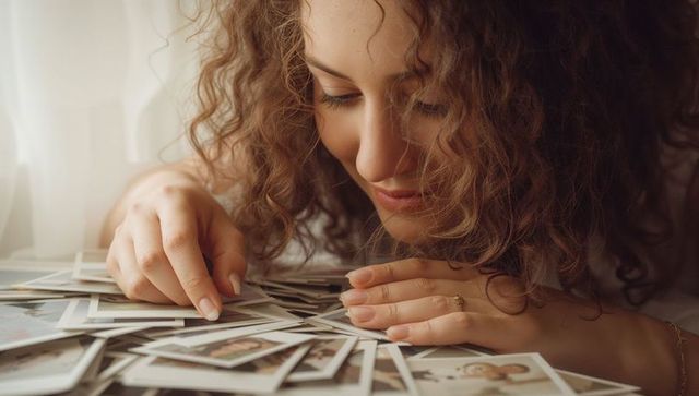 Curly woman examining vintage polaroids on table, reliving memories in warm daylight