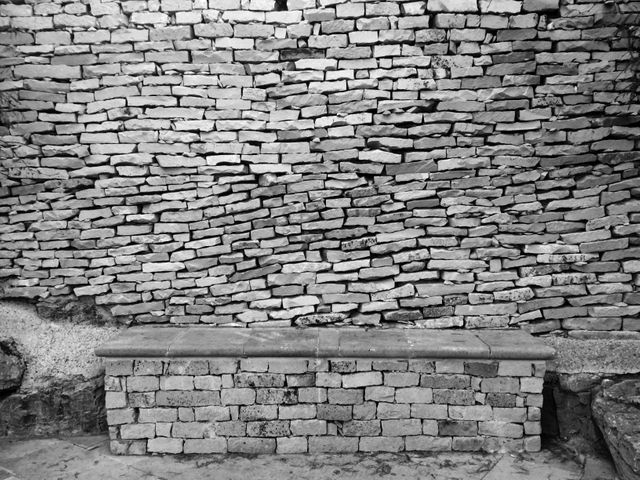 This vintage brick wall with a stone bench in black and white is suitable for backgrounds, architectural designs, and textures. It is useful for illustrating historical or rustic outdoor settings. Perfect for projects needing a classic, timeless look, or showcasing masonry work.