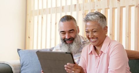 Happy Senior Couple Exploring Tablet on Couch Together