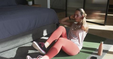 Woman doing ab crunches on yoga mat in sunlit bedroom morning home workout routine