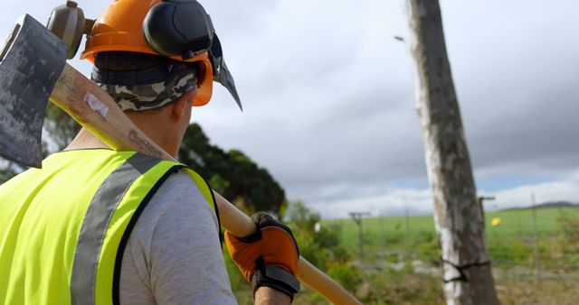 This image illustrates a lumberjack carrying an axe, wearing safety gear including a helmet and high-visibility vest, set in a forest area with an overcast sky. Ideal for use in articles or websites related to forestry, manual labor, outdoor work safety, environmental conservation, and industrial work activities.