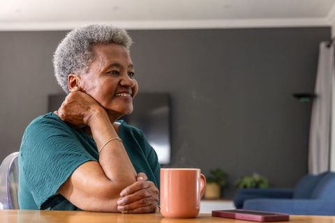 Senior african american woman smiling while drinking morning coffee with steaming mug at cozy home