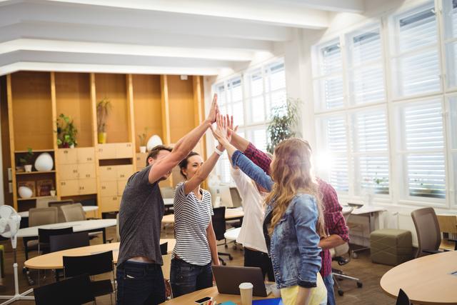Group of young business executives giving high five in a modern office. Ideal for illustrating concepts of teamwork, success, collaboration, and positive work environment. Suitable for business presentations, corporate websites, and motivational materials.
