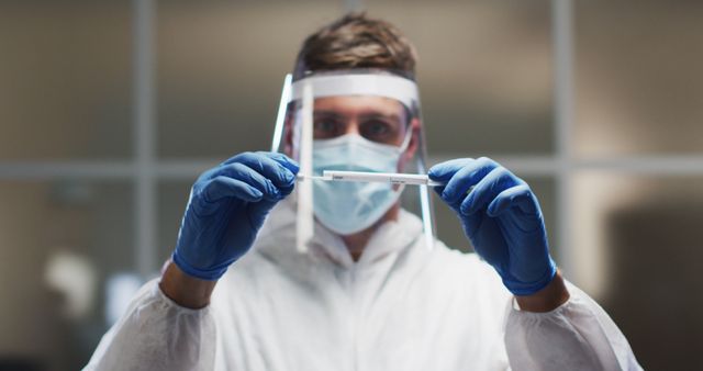 Caucasian male medical worker wearing protective clothing and face shield inspecting dna swab in lab. healthcare, medical research technology and hygiene during coronavirus covid 19 pandemic.