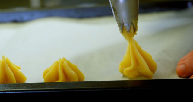 Close-up shot of dough being precisely piped onto a baking sheet by hand. Ideal for illustrating baking techniques, pastry preparation or detailed food craftsmanship. Great for cooking blogs, recipe books, and culinary tutorials.