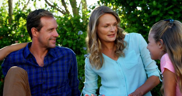 Parents and daughter chatting and smiling in garden. Ideal for content about family time, outdoor activities, happiness, bonding, and natural settings.