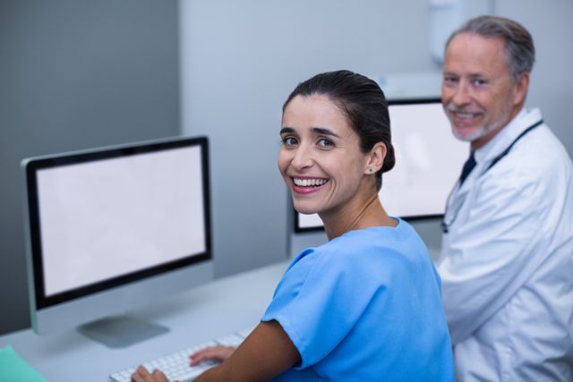 Doctor and nurse smiling while collaborating on computer in a hospital setting. Ideal for use in healthcare, medical teamwork, modern technology in healthcare, and hospital workplace imagery.