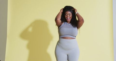 Confident woman in gray activewear adjusting hair on yellow background