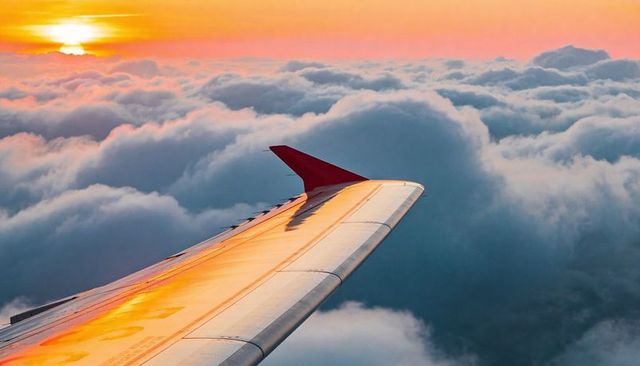 Sunrise Reflection on Airplane Wing Gliding Above Clouds with Red Winglet and Golden Sky