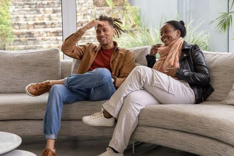 Relaxed african american couple conversing on light gray sectional sofa in sunlit living room