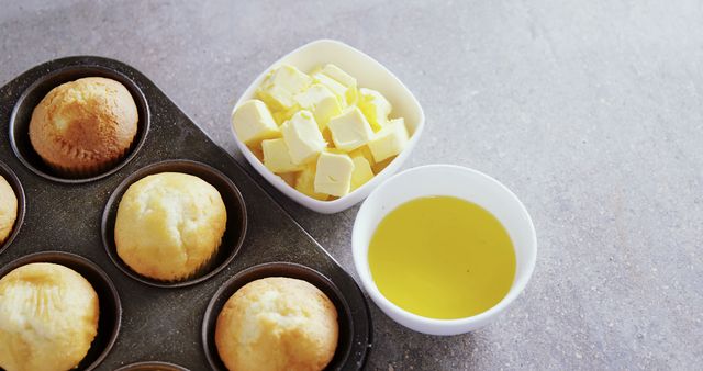 Freshly baked muffins sit in a muffin tin next to bowls of butter and melted butter, with copy space. A kitchen scene captures the ingredients and results of baking, suggesting a home cooking or recipe concept.
