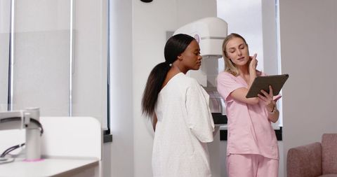Black Patient Consulting Caucasian Technologist in Pink Scrubs at Mammography Unit