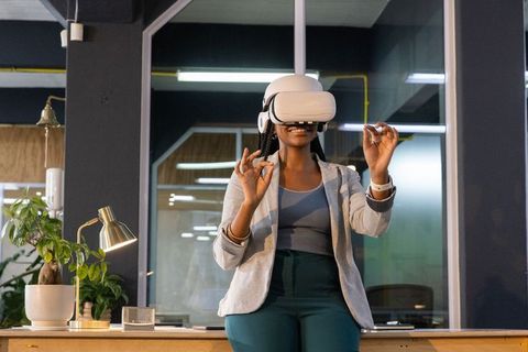 African american businesswoman wearing vr headset making pinch gestures in modern office