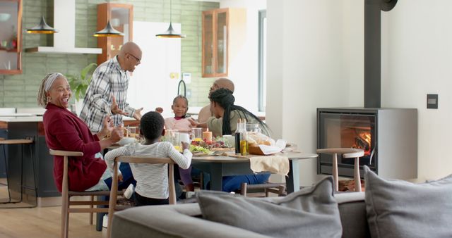 Family gathered around table enjoying meal in contemporary living space with fireplace. Suitable for themes of family bonding, modern lifestyle, home dining, and intimate moments. Ideal for advertisements, brochures, blogs, and social media highlighting family values and home living.