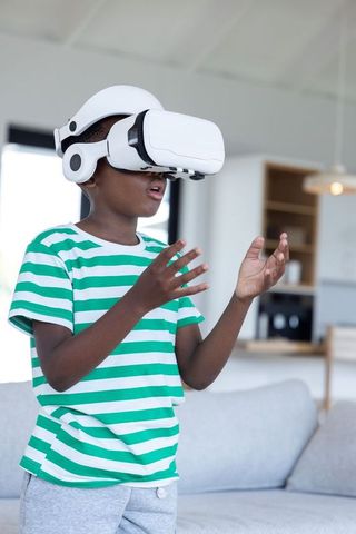 African american boy wearing vr headset reacting and reaching out in modern living room