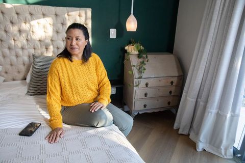 Mature woman sitting on bed edge wearing mustard sweater and olive pants in cozy bedroom